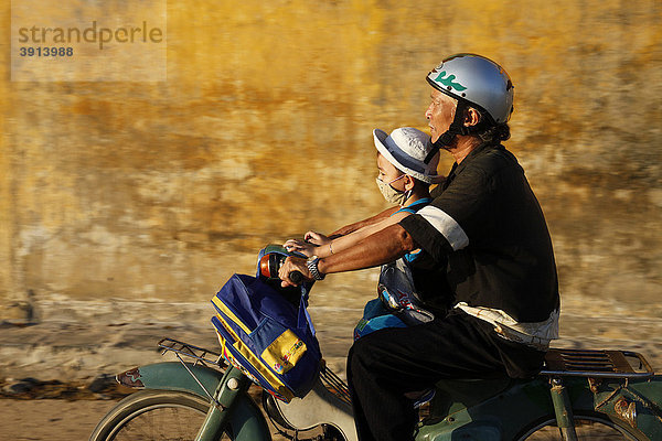 Ein vietnamesischer Vater mit seinem Sohn auf dem Motorroller mit Rucksack in Hoi An  Vietnam  Südostasien