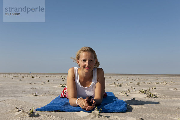 Junge Frau  20-25 Jahre  entspannt sich an einem strahlend blauen Sommertag am Sandstrand von St Peter Ording  Nordsee  Nordfriesland  Schleswig-Holstein  Norddeutschland  Deutschland  Europa
