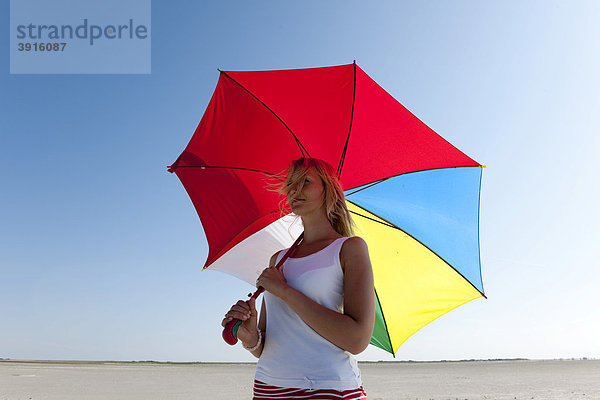 Junge Frau  20-25 Jahre  mit buntem Sonnenschirm am weiten Sandstrand von St Peter Ording  Nordsee  Nordfriesland  Schleswig-Holstein  Norddeutschland  Deutschland  Europa