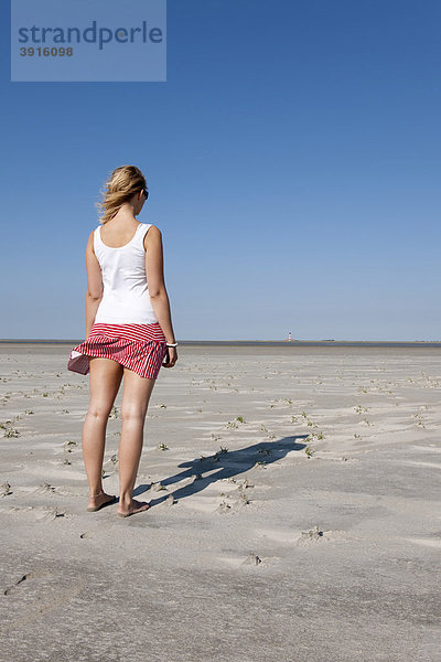 Junge Frau  20-25 Jahre blickt an einem sonnigen Sommertag am Sandstrand von St Peter Ording in die Ferne  Nordsee  Nordfriesland  Schleswig-Holstein  Norddeutschland  Deutschland  Europa