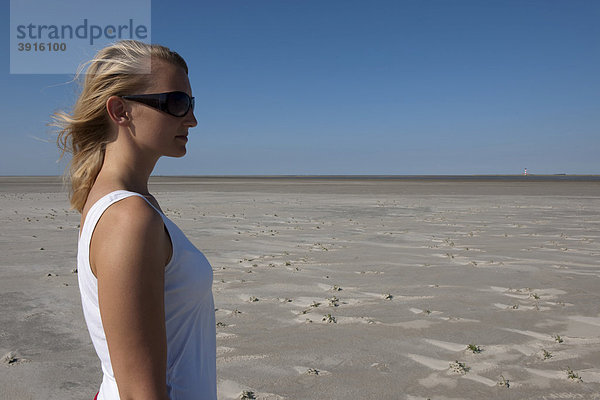 Junge Frau  20-25 Jahre blickt an einem sonnigen Sommertag am Sandstrand von St Peter Ording in die Ferne  Nordsee  Nordfriesland  Schleswig-Holstein  Norddeutschland  Deutschland  Europa