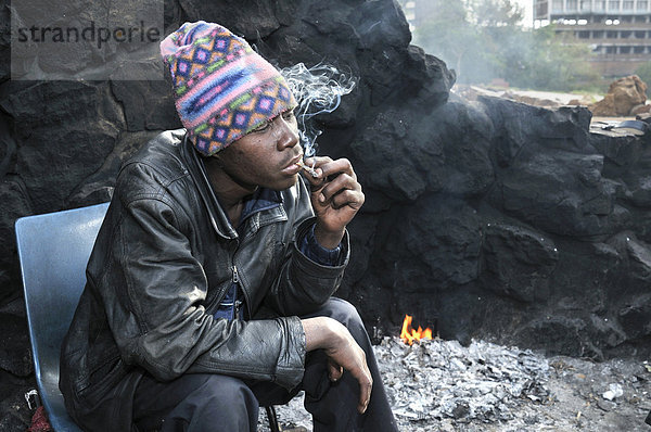 Obdachloser Immigrant aus Mosambik konsumiert Drogen  Marihuana  und wärmt sich am frühen Morgen an einem Feuer im Park Pullinger Kop  Stadtteil Hillbrow  sozialer Brennpunkt im Zentrum von Johannesbug  Südafrika  Afrika