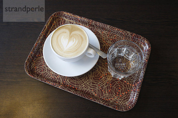 Tasse Cappuccino und ein Glas Wasser auf einem Tablett