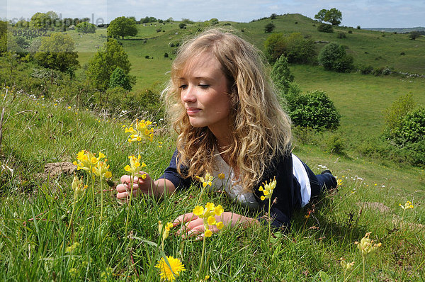 Junge Frau liegt in einer hügeligen Landschaft  betrachtet Blumen