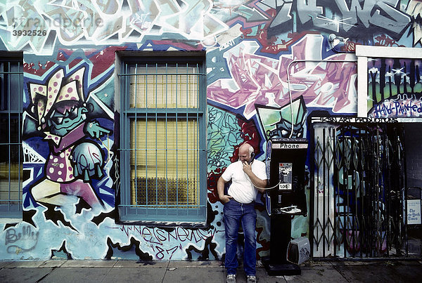 Mann telefoniert an einer Telefonsäule auf der Straße  Hauswand mit Graffiti bemalt  Hollywood  Los Angeles  Kalifornien  USA