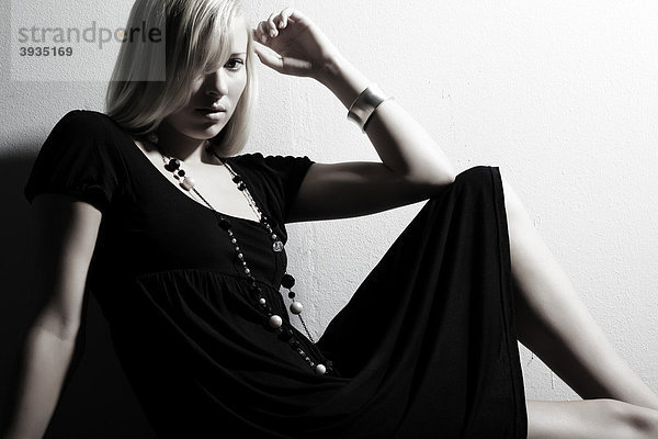 Portrait einer jungen Frau im schwarzen Kleid sitzend vor einer Wand mit Blick zum Betrachter