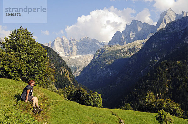 Frau sitzt im Gras mit Blick vom Bergdorf Soglio auf die Bondasca-Gruppe mit Sciora  Piz Cengalo und Piz Badile  Wanderweg Via Bragaglia und Sentiero Panoramico  Val Bregaglia  Tal des Bergell  Engadin  Graubünden  Schweiz  Europa