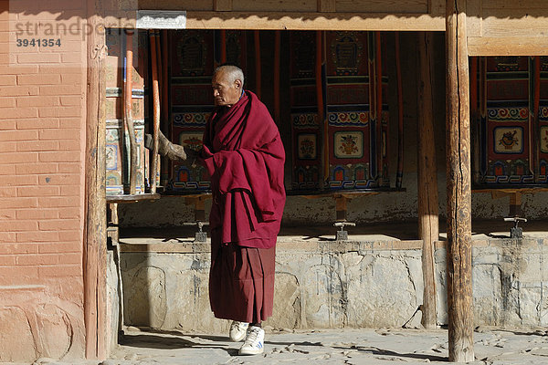 Tibetischer Mönch vor Gebetsmühlen aus Holz im Klosterrundgang  Kora  der tibetischen Klosteranlage Labrang  Xiahe  Gansu  China  Asien