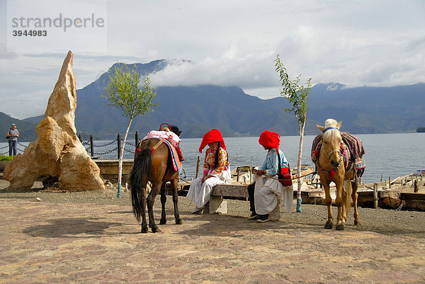 Ethnologie  Frauen der Mosu Ethnie in Tracht gekleidet mit Pferden am Ufer  Luoshui  Lugu Hu See  Provinz Yunnan  Volksrepublik China  Asien