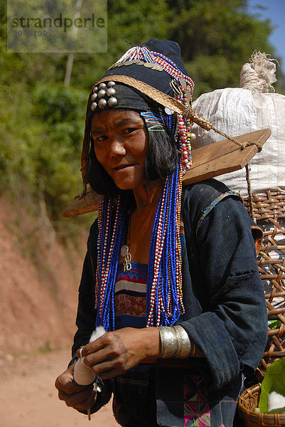 Armut  Portrait  Frau der Akha Djepia Ethnie  traditionelle bunte Kleidung  Haube als Kopfbedeckung  Spinnen von Baumwolle zum Faden  Tragen einer Last über Joch auf den Schultern  Ban Khay  Distrikt Boun Tai  Provinz Phongsali  Laos  Südostasien  Asien