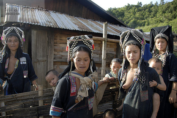 Armut  Frauen der Akha Nuqui Ethnie  Kleinkinder auf dem Rücken  Tracht  traditionelle Kleidung  Farbe Indigo  Kopfbedeckung mit Silber-Schmuck  vor Hütte  Dorf Ban Seochayneua  Provinz und Distrikt Phongsali  Laos  Südostasien  Asien