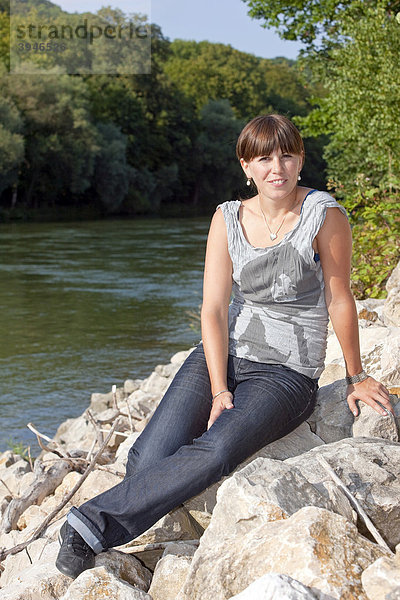 Eine junge Frau sitzt an einem Fluss