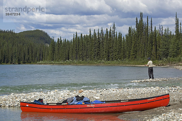 Zwei beladene Kanus am Ufer des oberen Liard River Flusses  dahinter ein angelnder Mann  Kiesbank  Yukon Territory  Kanada