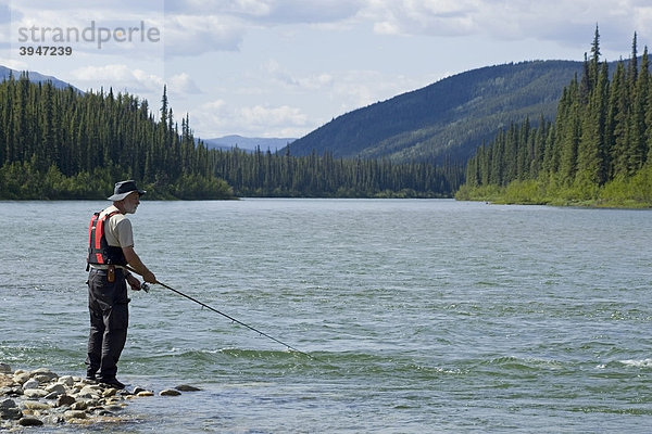 Mann angelt im oberen Liard River Fluss  steht auf einer Kiesbank  hinten Berge  Yukon Territory  Kanada