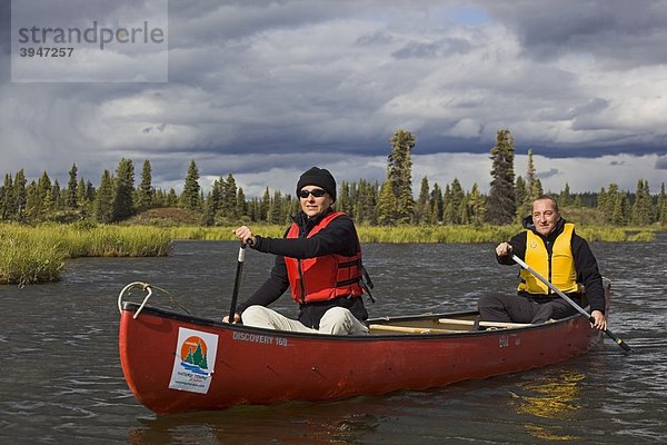 Paar  Mann und Frau paddeln im Kanu  Kanufahrt auf den Caribou Lakes Seen  dahinter Wolken  oberer Liard River Fluss  Yukon Territory  Kanada
