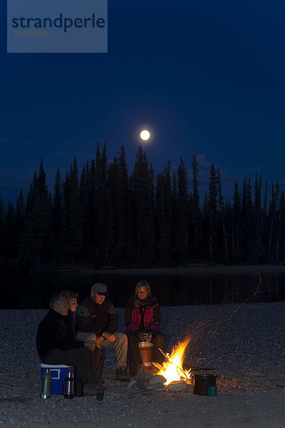 Menschen sitzen an einem Lagerfeuer  Vollmond dahinter  Mondlicht  Ufer des oberen Liard River Flusses  Yukon Territory  Kanada