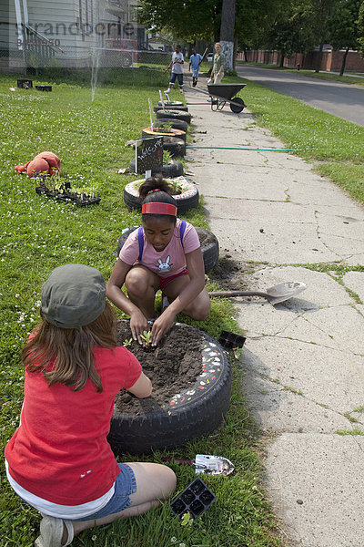 Zwei Mädchen pflanzen Blumen in alte Autoreifen  am Rand eines Gartens  in einem Programm namens Growing Healthy Kids für Kinder im Alter von 5-11 Jahren  in einem Earthworks Urban Garden Garten  in dem Nahrung für die Capuchin Soup Kitchen Suppenküche angebaut wird  Detroit  Michigan  USA