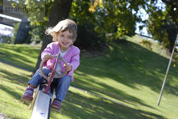 Zweieinhalb-jähriges Mädchen hat Spaß auf einer Wippe im Park