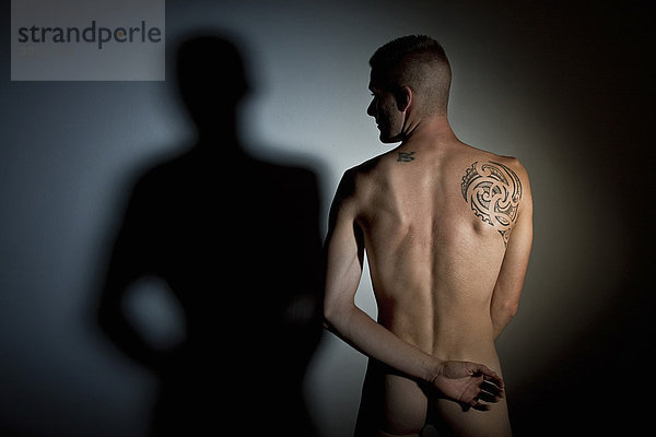 Akt junger Mann  Rückenansicht  Tattoo auf dem Schulterblatt  Arm auf dem Rücken verschränkt  Blick zur Seite