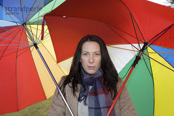 Junge Frau  30-35 Jahre  schützt sich mit zwei bunten Regenschirmen vor dem nasskaltem Winterwetter