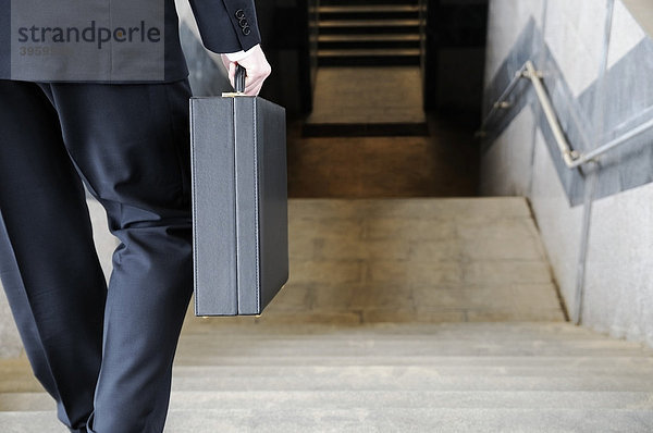Geschäftsmann mit Aktenkoffer geht Treppen einer U-bahnstation hinunter  Rückenansicht