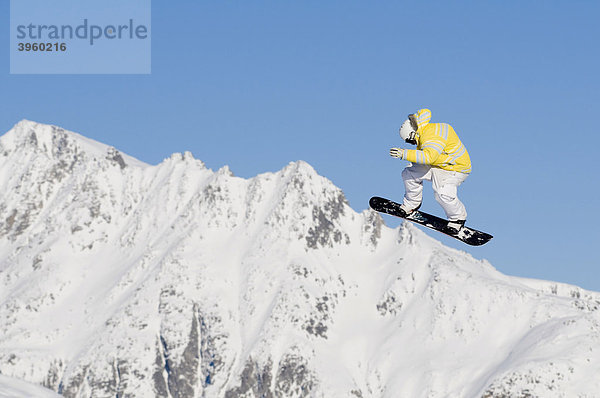 Skifahrer beim Sprung vor blauem Himmel  dahinter schneebedeckte Bergkette  Andermatt  Schweiz