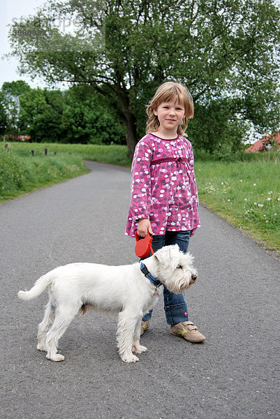 Fünfjähriges Mädchen mit Zwergschnauzer  weiß  unterwegs auf einem Feldweg