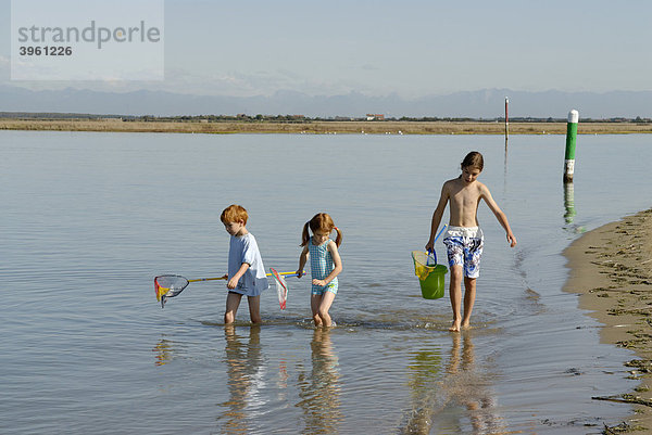 Kinder spazieren mit Fischernnetz und Eimer am Strand am Meer  Bibione  Adria  Venetien  Veneto  Italien  Europa
