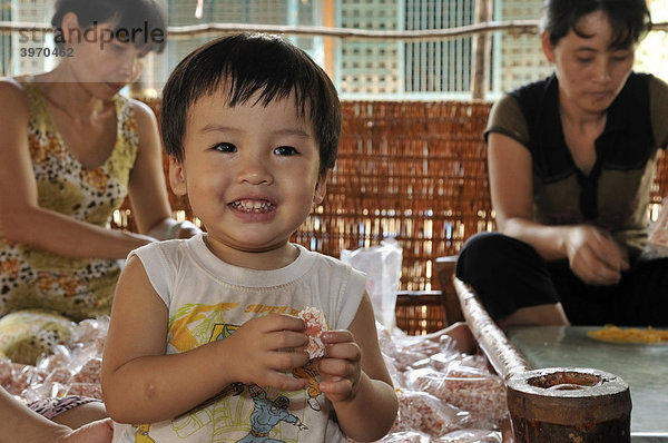 Kleines Kind lacht und isst Puffreis-Süßigkeiten  Süßwarenfabrik  Vinh Long  Mekongdelta  Vietnam  Südostasien