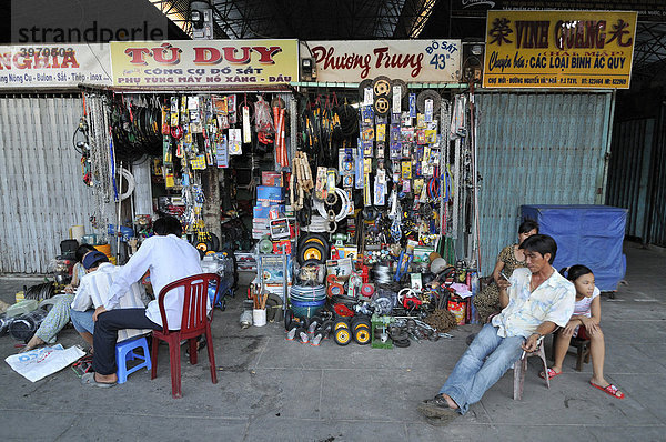 Familie sitzt vor einem Geschäftslokal am Markt  Eisen- und Haushaltswarenladen  Mann spielt mit Mobiltelefon Vinh Longh  Mekongdelta  Vietnam  Asien
