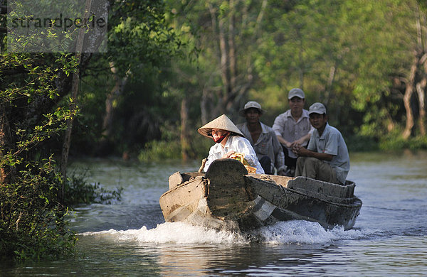Eine Frau mit traditionellem vietnamesischem Kegelhut fährt ein Boot auf dem Mekong  hinten drei Männer  Vinh Long  Mekongdelta  Vietnam  Asien