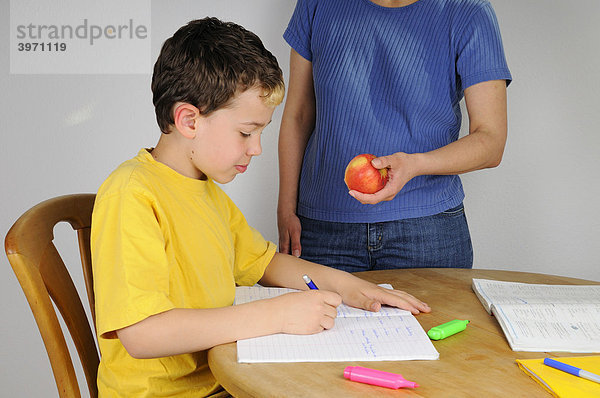 Junge macht Hausaufgaben für die Schule  Mutter bietet einen Apfel an