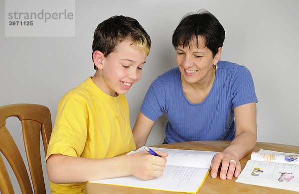 Junge macht Hausaufgaben für die Schule  Mutter unterstützt ihn dabei  beide lachen
