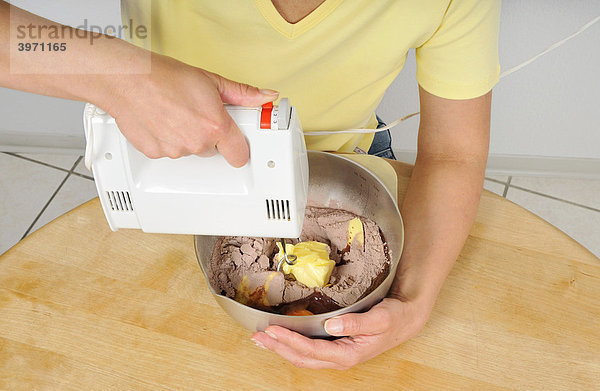 Frau mit Handmixer beim Zubereiten eines Teiges für einen Kuchen