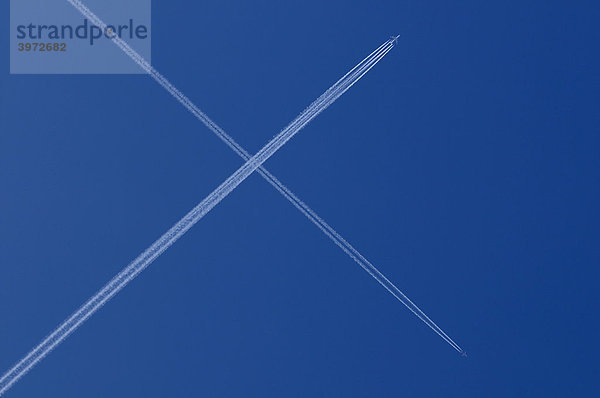 Zwei Flugzeuge mit Kondensstreifen kreuzen sich am blauen Himmel  X