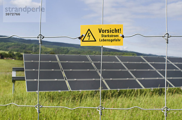 Photovoltaik  Module auf Ständer hinter Schutzzaun mit Warntafel  Vorsicht Starkstrom Lebensgefahr