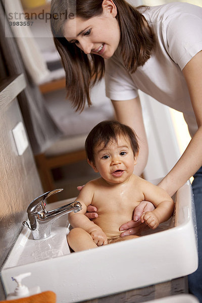 Mutter badet Baby  9 Monate  im Waschbecken