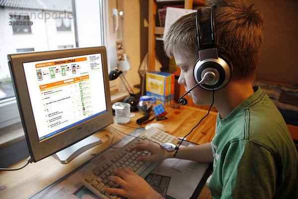 Junge  13 Jahre alt  surft mit seinem Computer zuhause im Internet auf einer Chat-Seite für Jugendliche  per Headset kann er mit anderen Chatteilnehmern reden