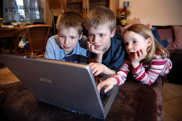 Geschwister  7  11  13 Jahre alt  mit Laptop Computer  im Wohnzimmer  spielen ein Lernspiel Quiz