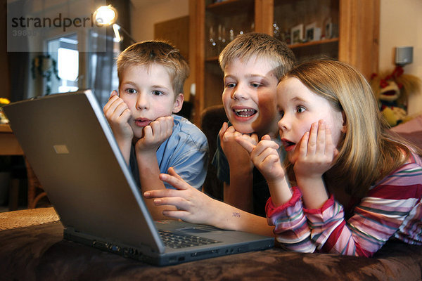 Geschwister  7  11  13 Jahre alt  mit Laptop Computer im Wohnzimmer  spielen ein Lernspiel Quiz