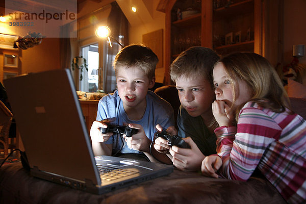 Geschwister  7  11  13 Jahre alt  mit Laptop Computer im Wohnzimmer  spielen ein Autorennen Computerspiel