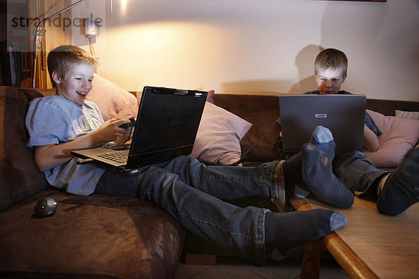 Brüder  11 und 13 Jahre alt  mit Laptop Computer im Wohnzimmer  spielen ein Autorennen Computerspiel auf zwei Rechnern gegeneinander