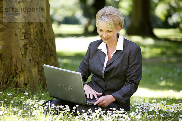 Frau im Business Kostüm  Hosenanzug  Geschäftsfrau  Anfang 40  arbeitet in einem Park an einen Laptop Computer