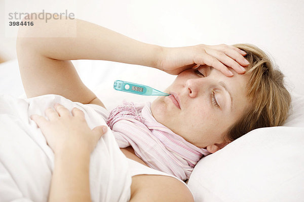 Junge Frau  krank im Bett  mit Fieber  misst die Körpertemperatur mit einem digitalen Fieberthermometer
