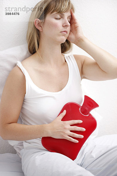 Junge Frau hat Bauchschmerzen  lindert die Beschwerden mit einer Wärmflasche
