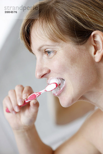 Junge Frau putzt sich in einem Badezimmer die Zähne