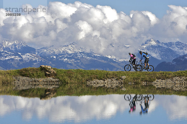 Mountainbike-Fahrerin und -Fahrer spiegeln sich im Wasserreservoir Salvensee an der Hohen Salve  Tirol  Österreich