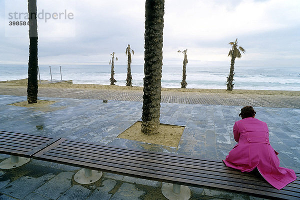 Einsame Frau in pinkfarbigem Mantel sitzt auf einer Bank und schaut aufs Meer  Promenade  Barcelona  Spanien  Europa