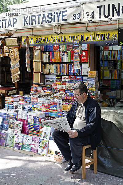 Buchhändler sitzt vor seinem Stand  liest Zeitung  Bücherbasar  Beyazit-Platz  Istanbul  Türkei