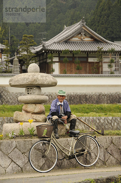 Alter Bauer mit Hacke und Fahrrad vor einer Steinlampe und traditionellem Haus in Ohara bei Kyoto  Japan  Asien